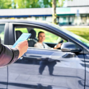 a hand with a phone in front of a car with a woman driving